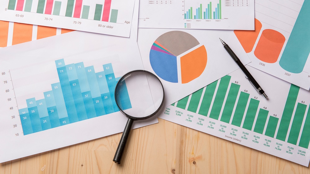 Magnifying glass and documents with analytics data lying on wood table