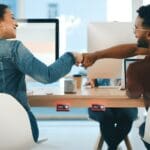 Rearview shot of two young designers giving each other a fist bump in an office, on display is Crestron desk scheduling device