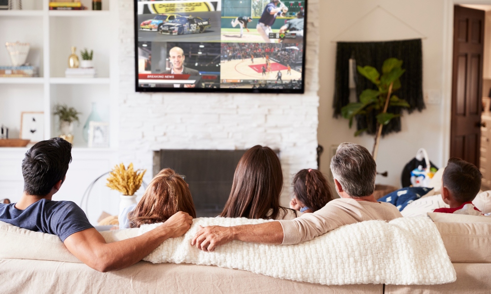 Back view of three generation Hispanic family sitting on the sofa watching TV. TV has AC-MV-41 video tilling solution so all can view different shows at the same time.