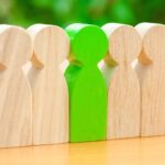 Wooden figures of people. Green man stands out from the crowd of workers. The concept of choosing a new leader. Choice of person. Hiring and recruiting. Talented employee. Selective focus