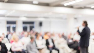 A keynote speaker at a business event, blurred for dramatic effect.