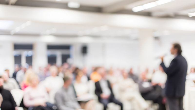 A keynote speaker at a business event, blurred for dramatic effect.