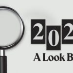 Minimalist design with a magnifying glass highlighting bold “2025” text and “A Look Back” below, set on a clean light gray background, symbolizing review, reflection, and analysis.