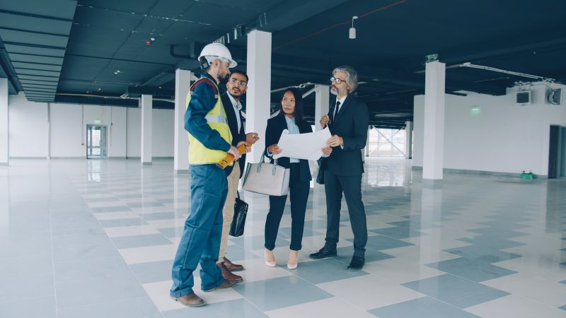 portrait of business team talking about maintenance of industrial building with glass walls and spacious halls. People and talks concept. silverkblack / stock.adobe.com