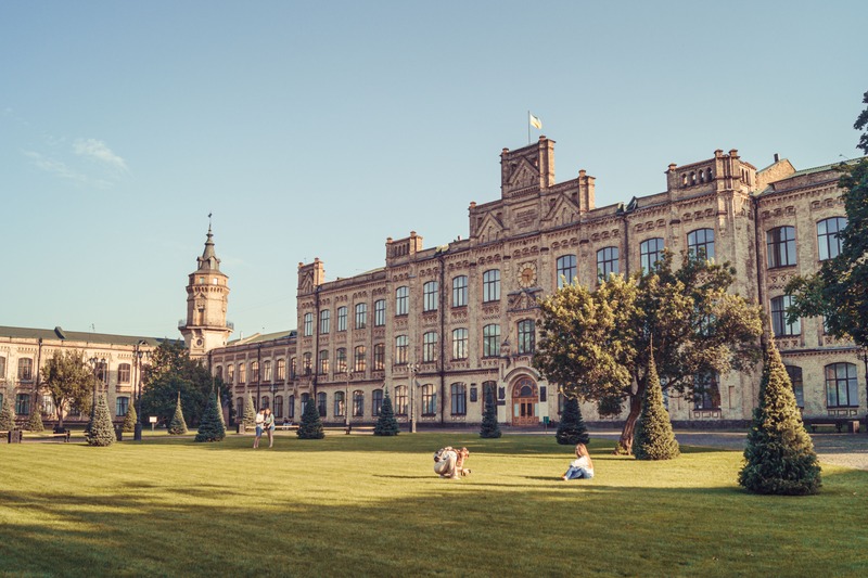 Historic university campus building exterior with green lawn and students
